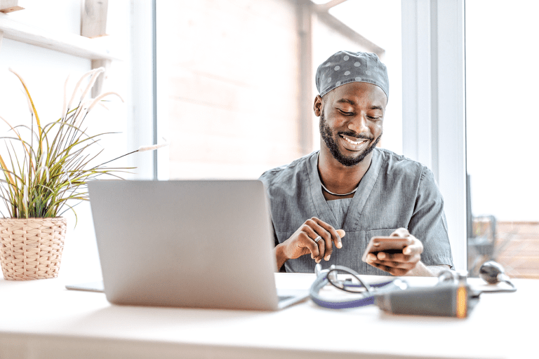 Healthcare Profession Sitting at His Desk, Smiling and Looking at Phone to Use for Digital Ordering Food